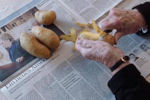 Eine ältere Frau schält über einer Zeitung Kartoffeln