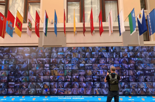 Bruno Kaufmann im Moskauer Fernsehstudio vor einer Wand mit Fernsehbildschirmen